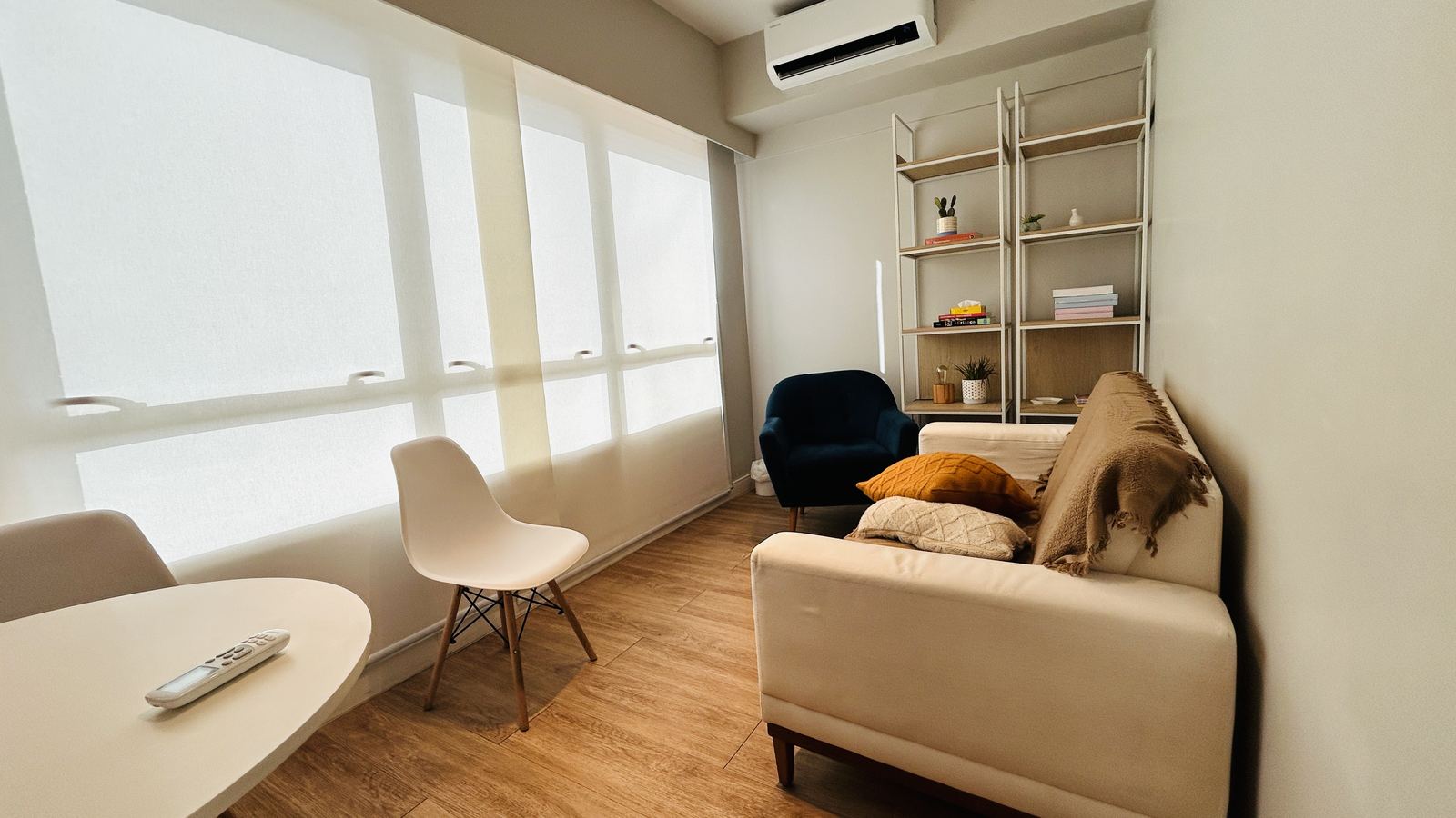 Sala Horizonte: sofá claro, poltrona azul, mesa redonda branca e janela ampla com persiana