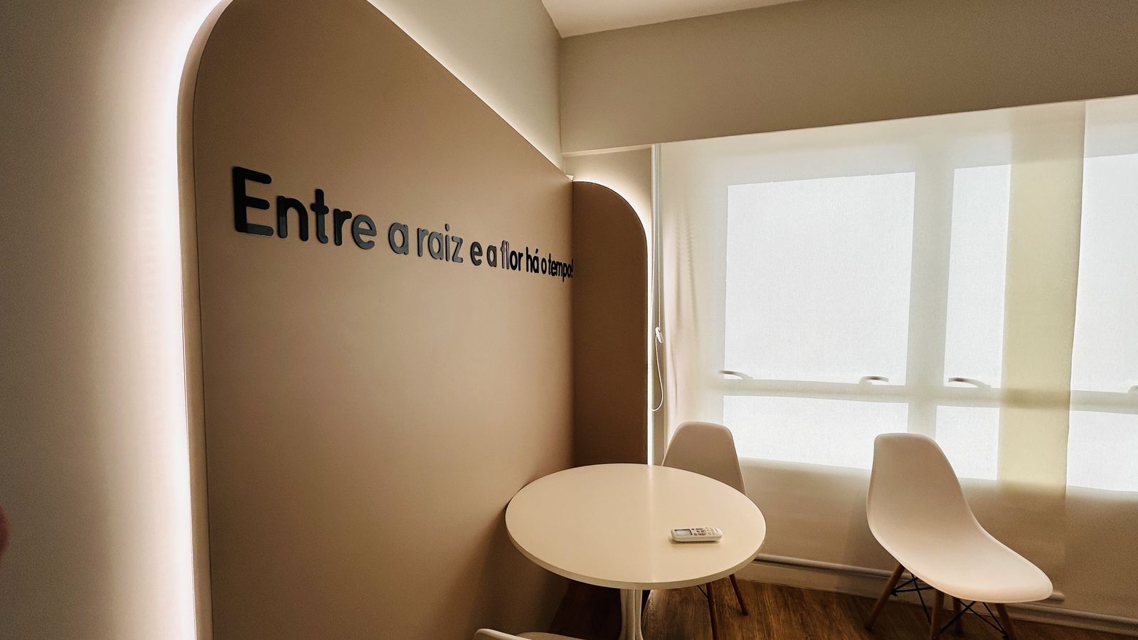 Sala Horizonte: parede curva com luz indireta, mesa redonda branca e cadeiras diante da janela